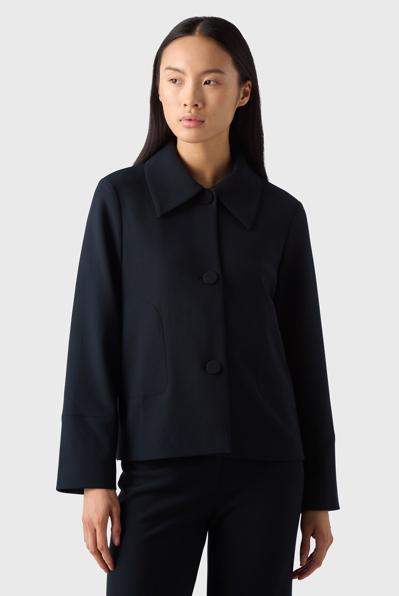 A woman wearing a navy Alba Crèpe Jacket with a classic collar, the jacket has long sleeves and is paired with black trousers.